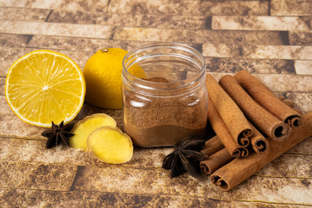 Jar with homemade spice paste, lemon and cinnamon on rustic surface. Healthy winter food concept....