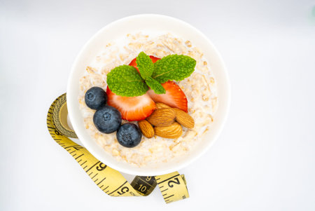 Healthy oatmeal bowl with fresh berries, nuts, and mint, next to a measuring tape. Perfect for diet and fitness related content. High quality photoの写真素材
