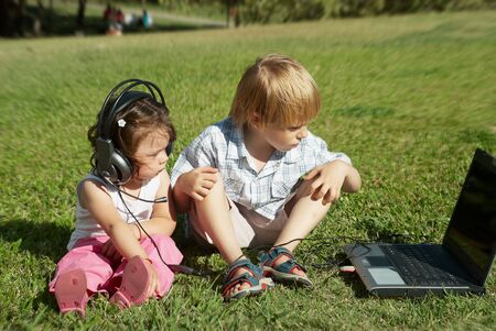 boy and a girl with laptop and headphones in the park on the grassの写真素材