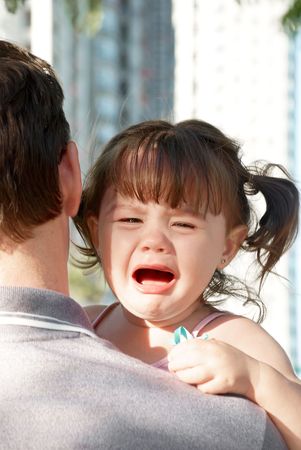 young girl crying on her father's shoulderの写真素材