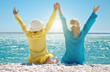 Beautiful girls with arms raised sitting on beachの写真素材