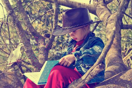 girl reading a book while sitting up in a tree.の写真素材