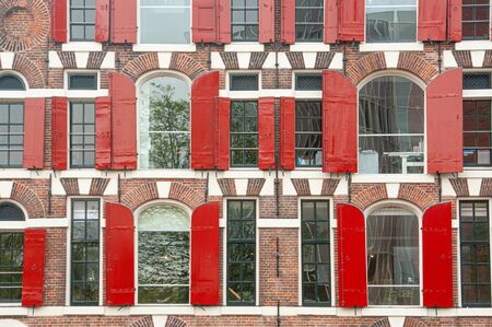 Front view of vintage windows with red wooden shutters of traditional houseの写真素材