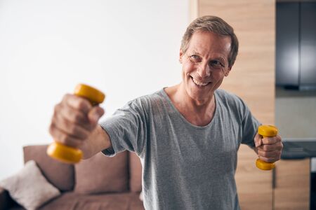 Kind mature man lifting dumbbells with pleasureの写真素材