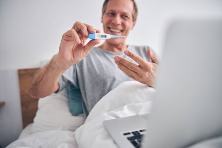 Close up of pleased man showing his thermometerの写真素材