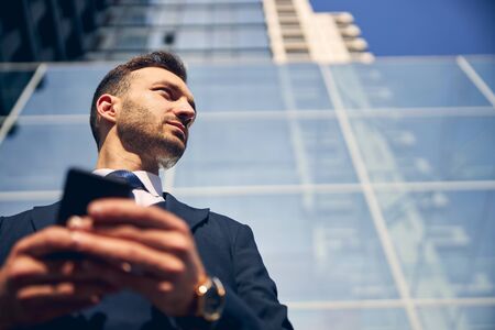 Young brunette man staying outside with smartphoneの写真素材