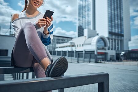 Dark-haired woman with a smartphone sitting outdoorsの写真素材