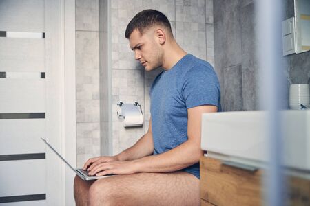 Handsome brunette male without trousers working in bathroomの写真素材