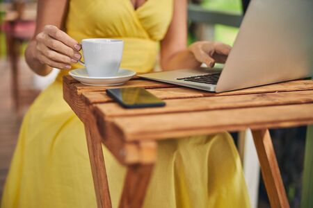 Cropped photo of a Caucasian woman with a cup of coffee typing on the laptopの写真素材