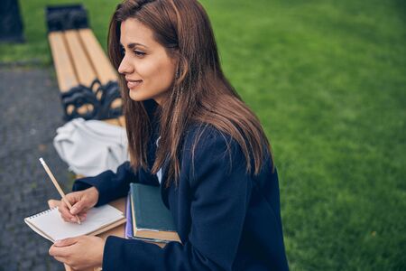 Beautiful lady with long dark hair sitting on bench with books