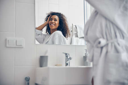 Joyful curly-headed young lady admiring her looksの写真素材