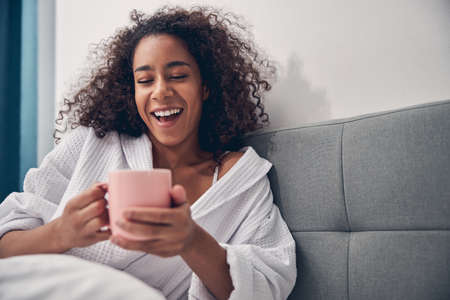 Dark-haired pretty lady laughing heartily in bed