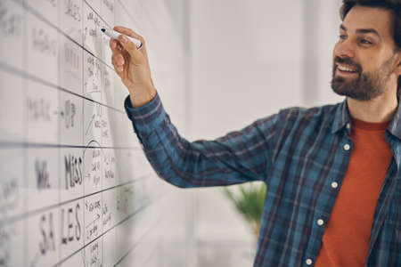 Handsome male worker writing on whiteboard in officeの写真素材