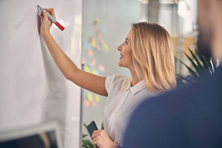 Charming young woman writing on whiteboard at workの写真素材