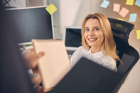 Joyful young woman giving documents to male colleague