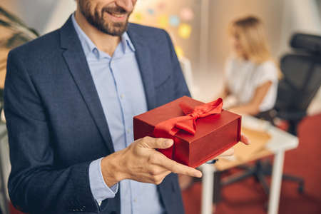 Young man holding red gift box with elegant ribbonの写真素材