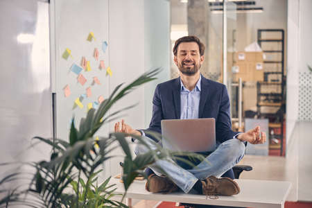 Handsome young man with laptop meditating at work