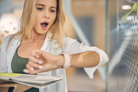 Shocked young woman checking time at workの写真素材