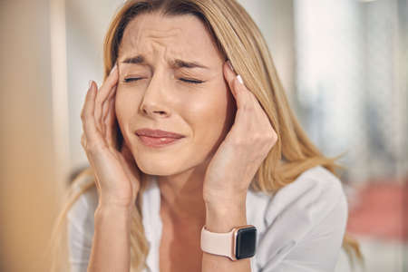 Unhappy young woman touching temples while having headache