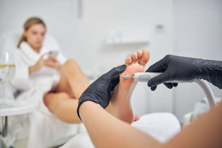 Young woman using smartphone during hardware pedicureの写真素材