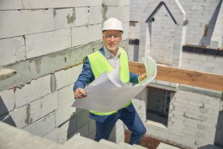 Smiling constructor in eyeglasses standing on the stairs