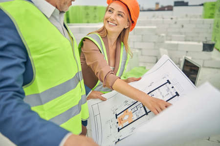 Joyful businesswoman analyzing a technical drawing with a foreman