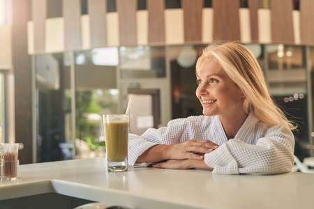 Cheerful lady standing at the bar with glass of juiceの写真素材