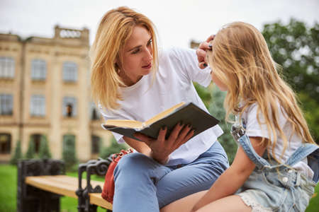 Mother touching hair of little girl while sitting in the city park