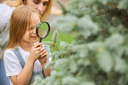 Young girl holding lens in hands while spending time with teacher in the park