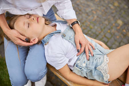 Female child wearing denim romper relaxing with mother in the outdoorsの写真素材