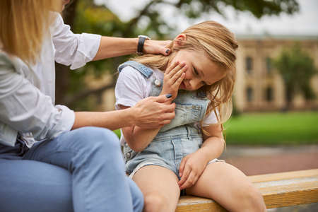 Mother with daughter sitting in the park on wooden benchの写真素材
