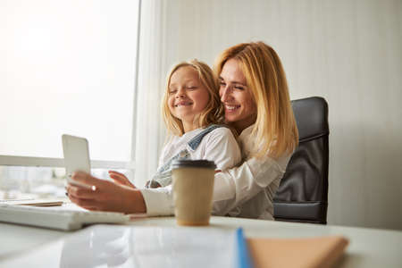 Smiling girl with pretty mother taking selfie on mobile phoneの写真素材