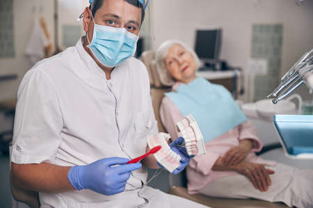 Young handsome orthodontist and woman patient sitting in dental clinic