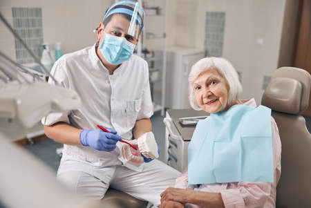 Young doctor in uniform is telling about hygiene of teeth in dental office