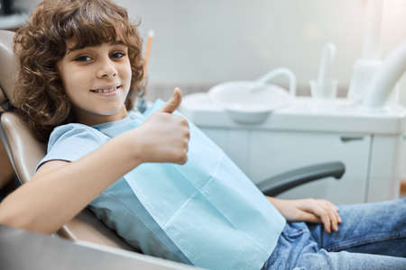 Positive-looking kid holding thumbs up in a dental clinicの写真素材