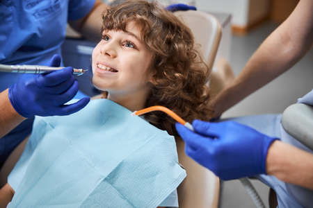 Cheerful kid smiling at a dentist with a dental drill