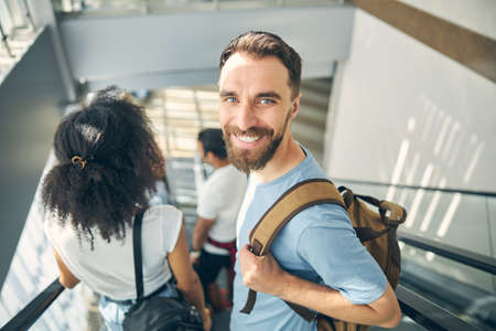 Happy smiling bearded man on moving staircase in international airport