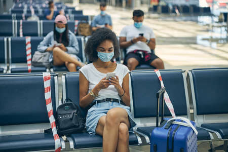 Woman using mobile phone at the airport sitting on the benchの写真素材
