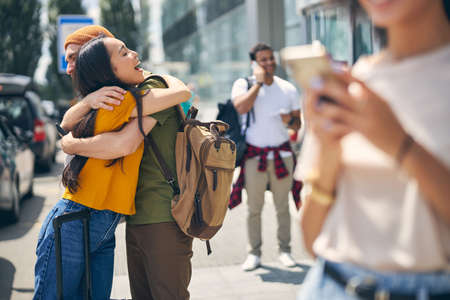 Smiling woman and man hugging in the outdoors with people on background