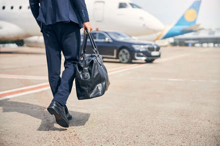 Businessman with a carry-on walking towards an aircraftの写真素材