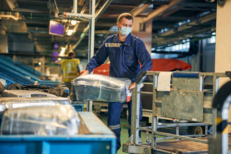 Man in an overall putting a suitcase on a trolleyの写真素材