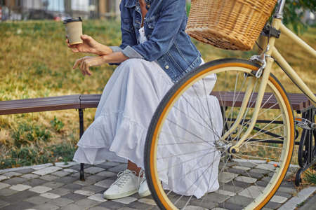 Cropped head portrait of stylish female in white long dress sitting on the bench in city parkの写真素材