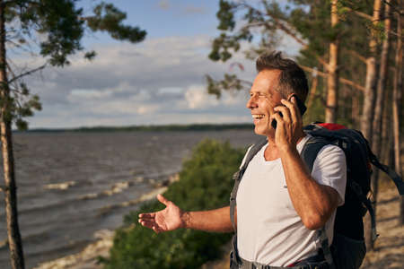 Cheerful male talkin on smartphone while hikingの写真素材