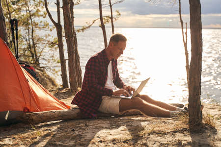Cheerful man using laptop during camping in natureの写真素材