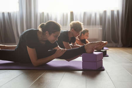 Smiling slim sportswoman stretching legs on mat in gymの写真素材
