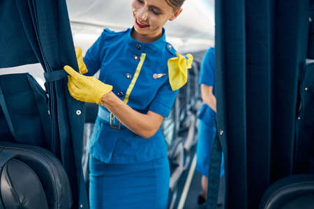 Very friendly woman flight attendant in yellow gloves standing in the empty hall of salon commercial planeの写真素材
