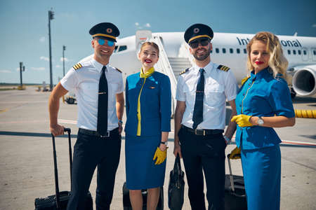 Cheerful airline workers standing in airfield before the flightの写真素材