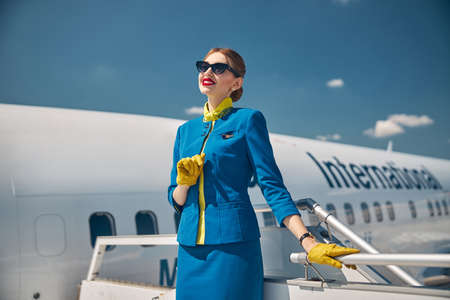 Cheerful stewardess in sunglasses standing on airplane stairsの写真素材