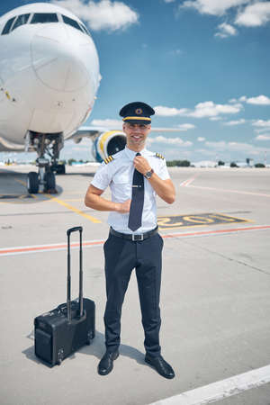 Handsome male pilot adjusting his tie at airportの写真素材