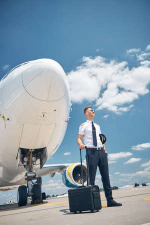Handsome pilot with travel bag standing by the plane